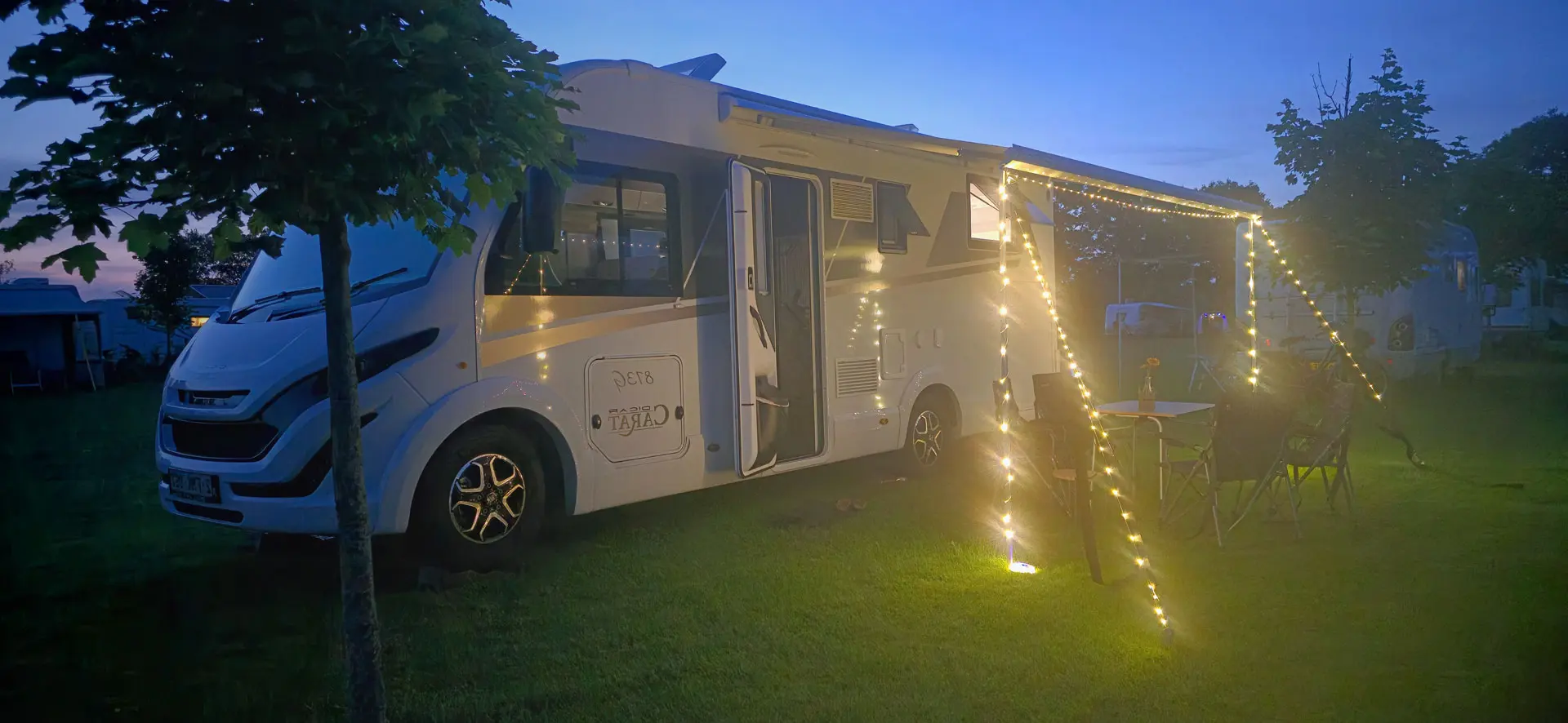 Luxe integraal camper onder luifel met lichtslinger bij zonsondergang